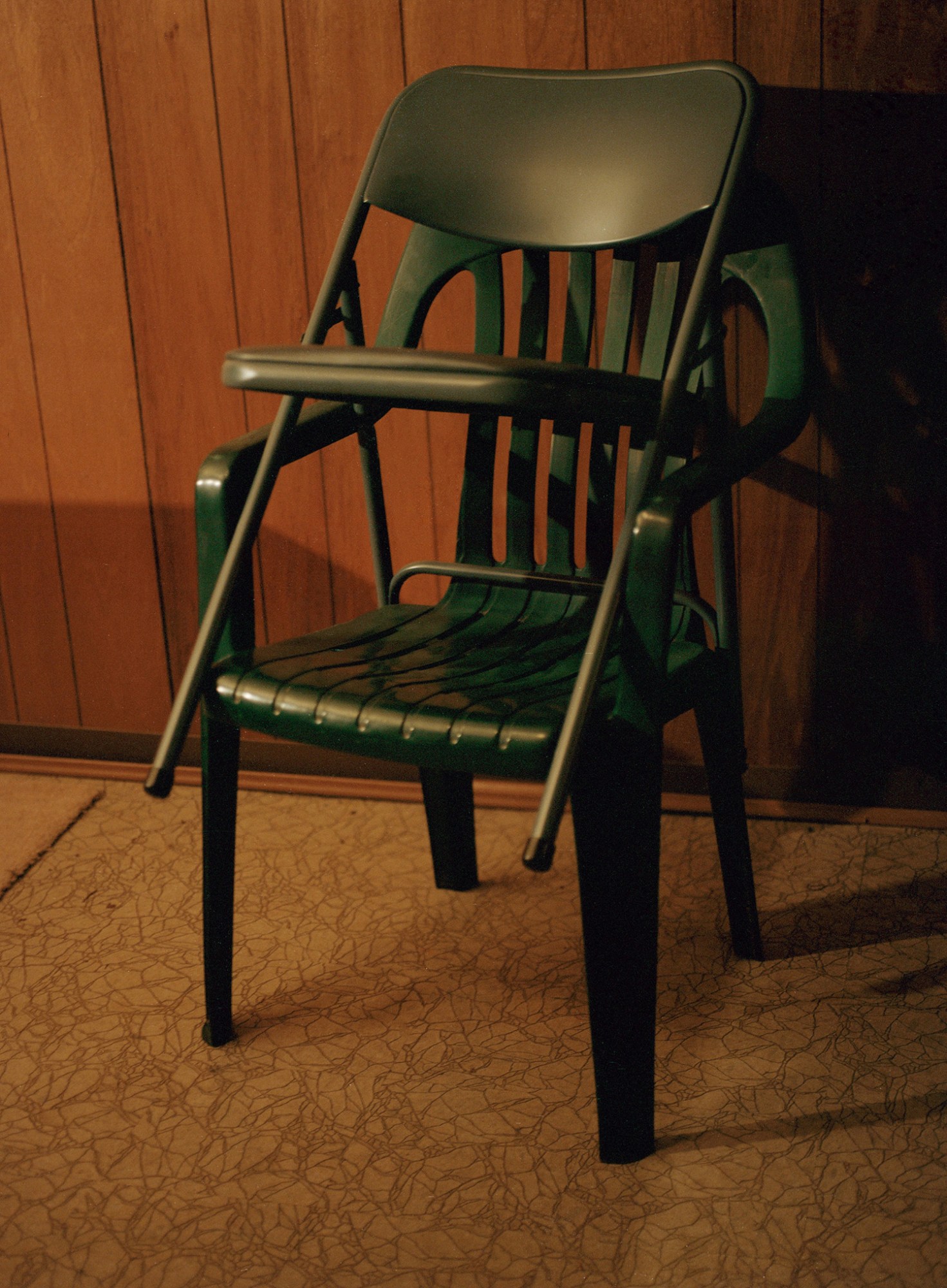 Two green plastic chairs stacked on top of one another in a yellow toned basement