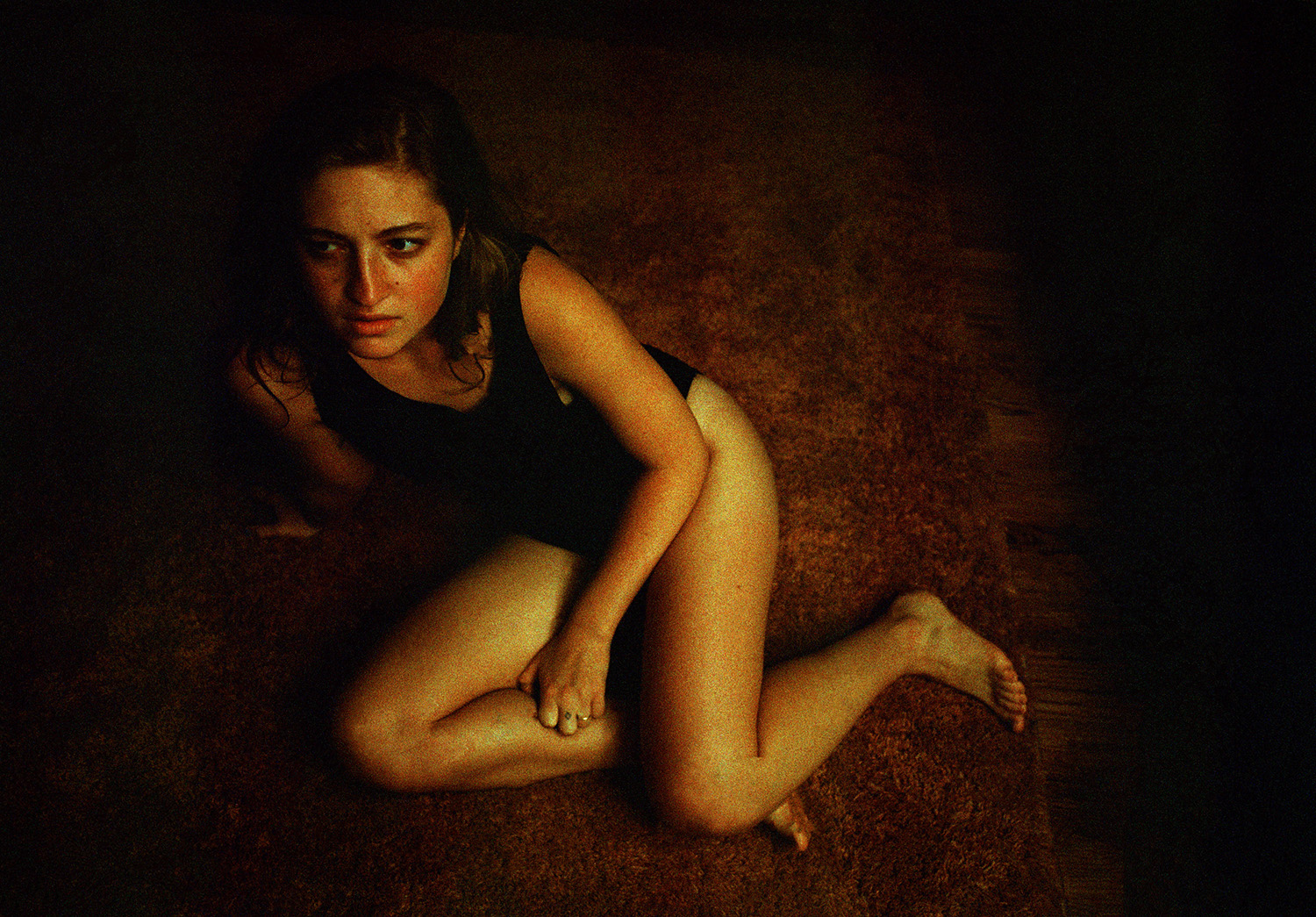 A blurry image of a person in a black tank top sitting on a brown carpet