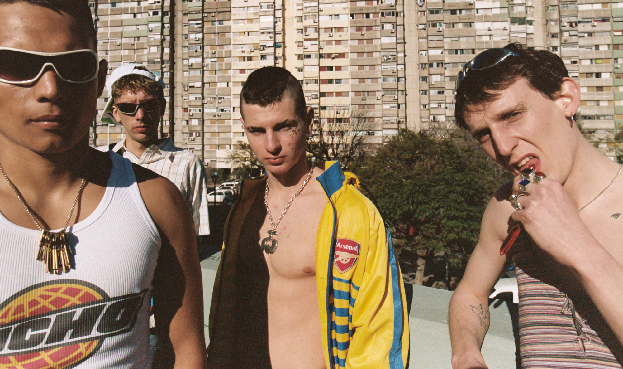 four young boys looking into the camera standing in front of a humoungous apartment building