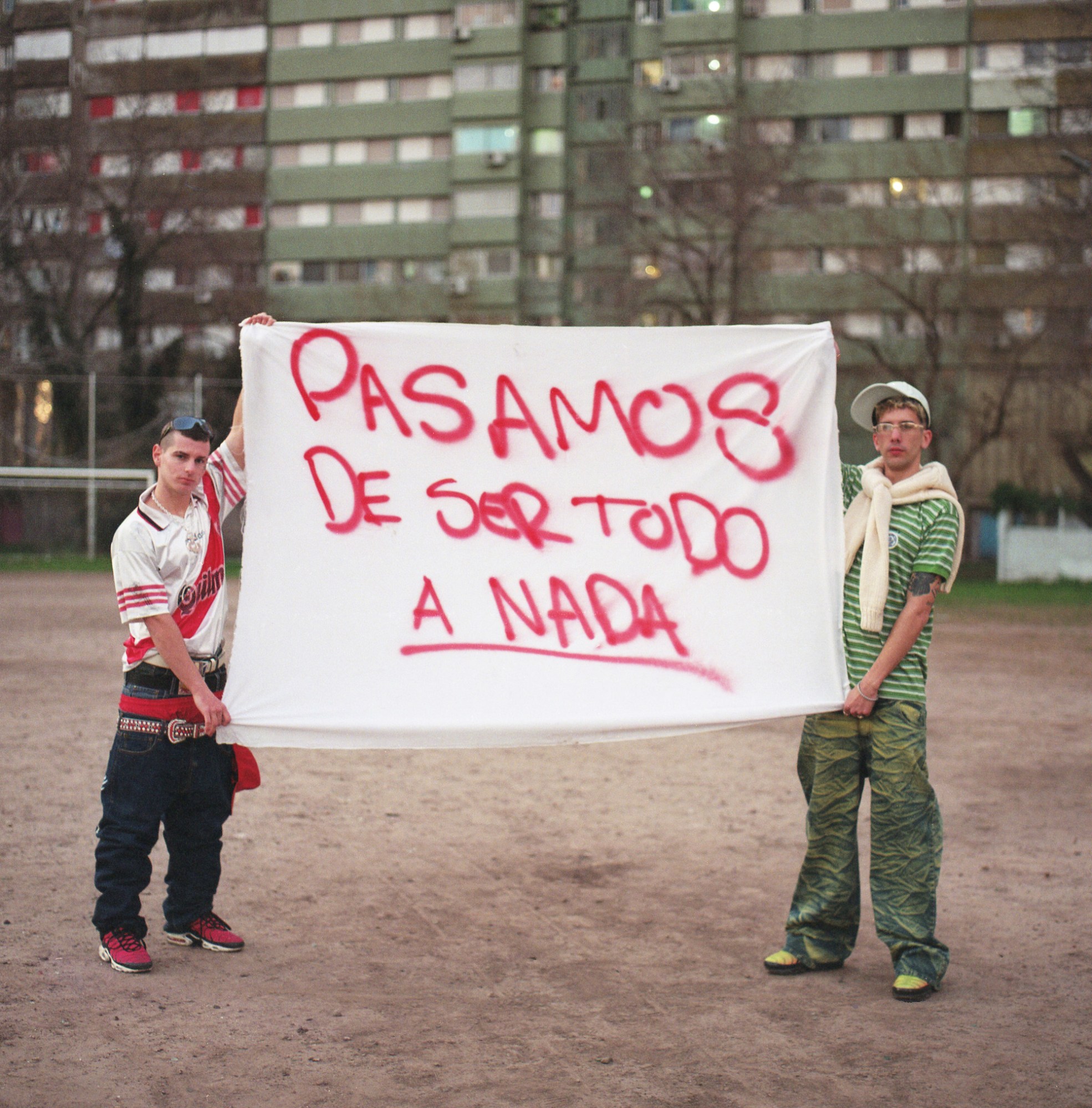 two men in polo shirts and baggy pants holding a sign with red lettering