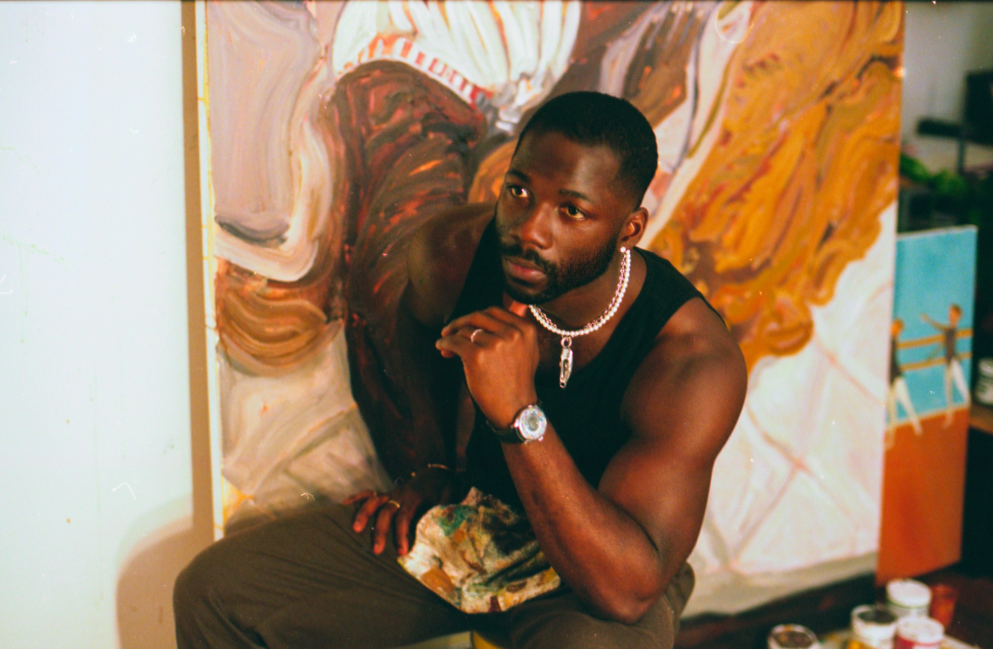 a closer crop of the artist Ludovic Nkoth sitting, holding his chin, in front of a colourful canvas