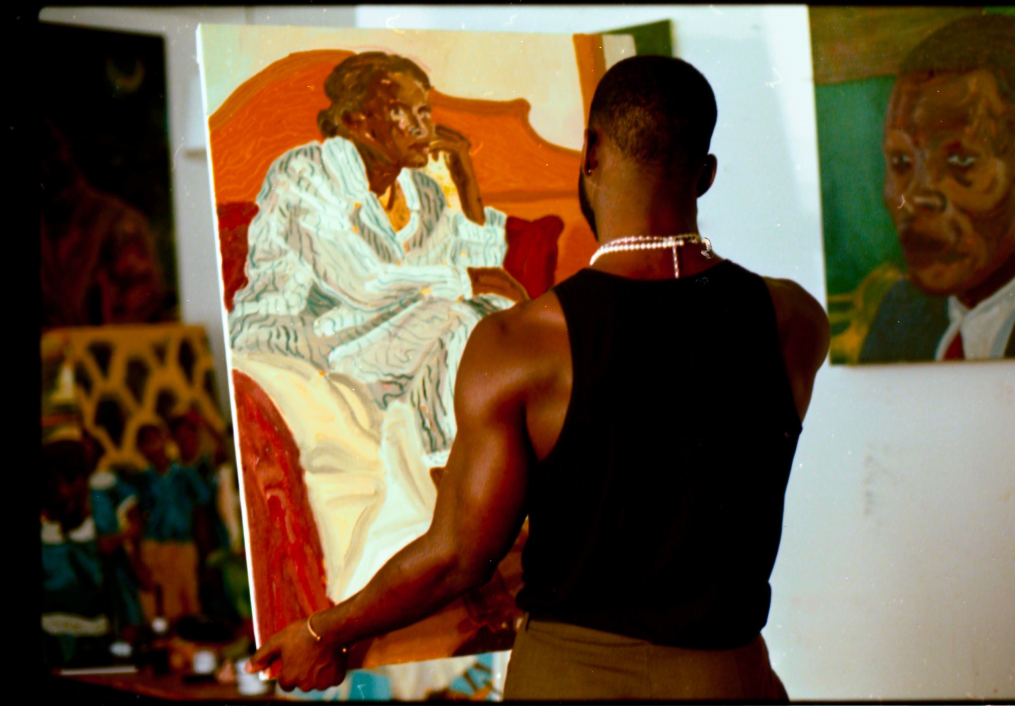 the artist Ludovic Nkoth pictured from behind, holding a canvas of an older seated lady wearing a patterned dress