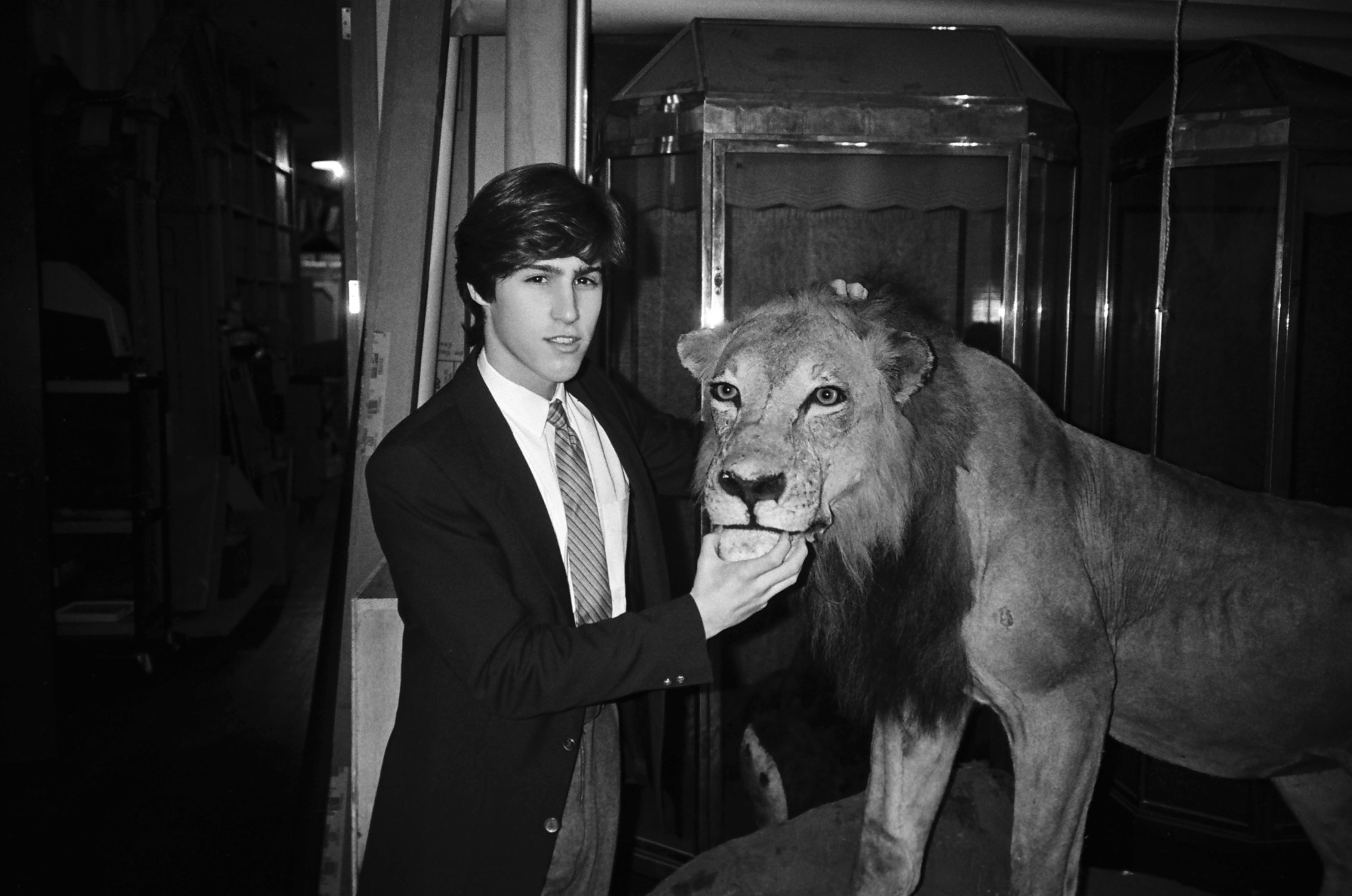 patrick mcmullan photo of pieter estersohn, a white man wearing a suit pretending to feed a taxidermy lion