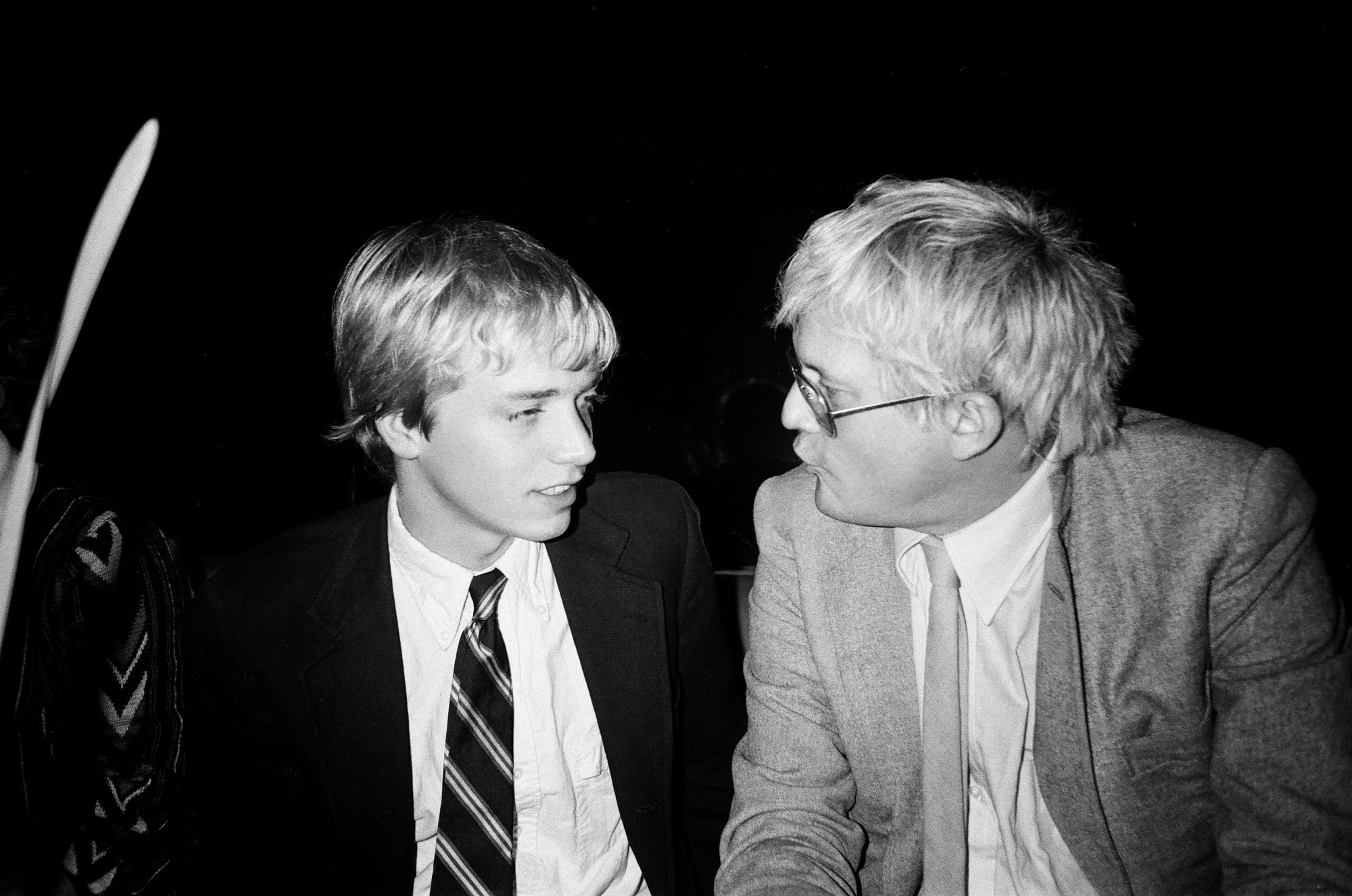 ian falconer, a blonde young man wearing a suit and tie, talks to david hockney, wearing a suit jacket and glasses.