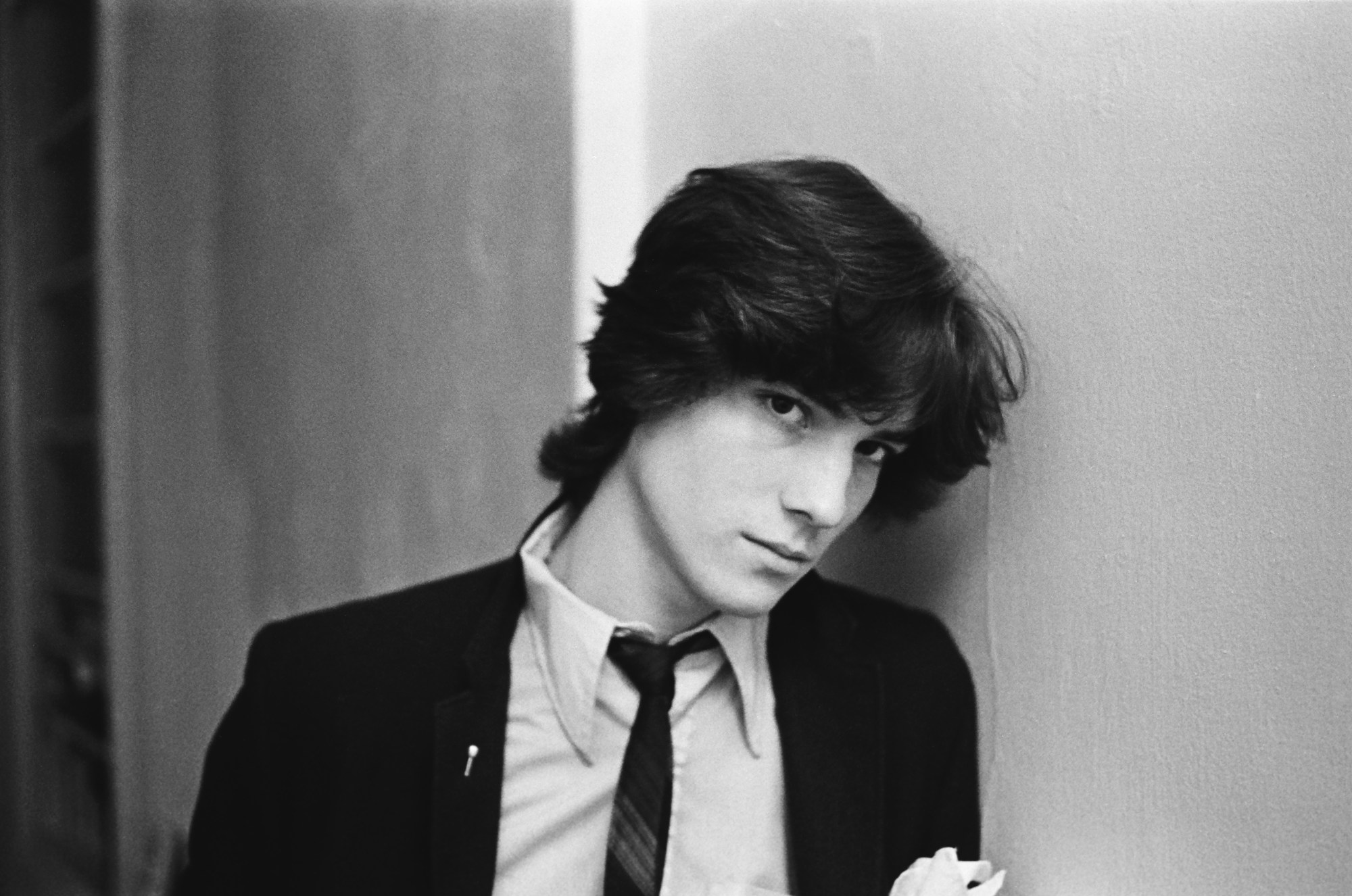 patrick mcmullan photo of a handsome man with dark medium length hair looking into the camera. he wears a suit jacket.