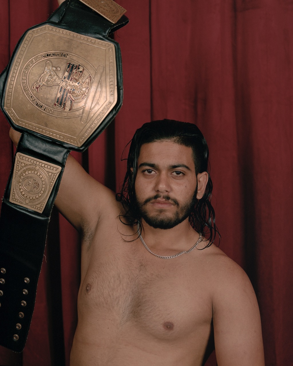 a wrestler holding a prize belt in front of a red curtain