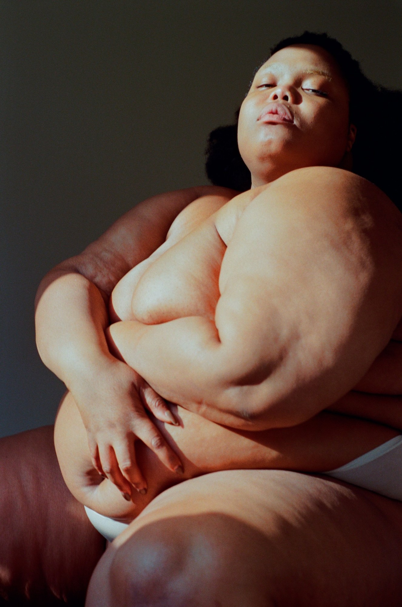 a seated plus size model in a pair of white briefs poses with her arms across her front in the sunlight