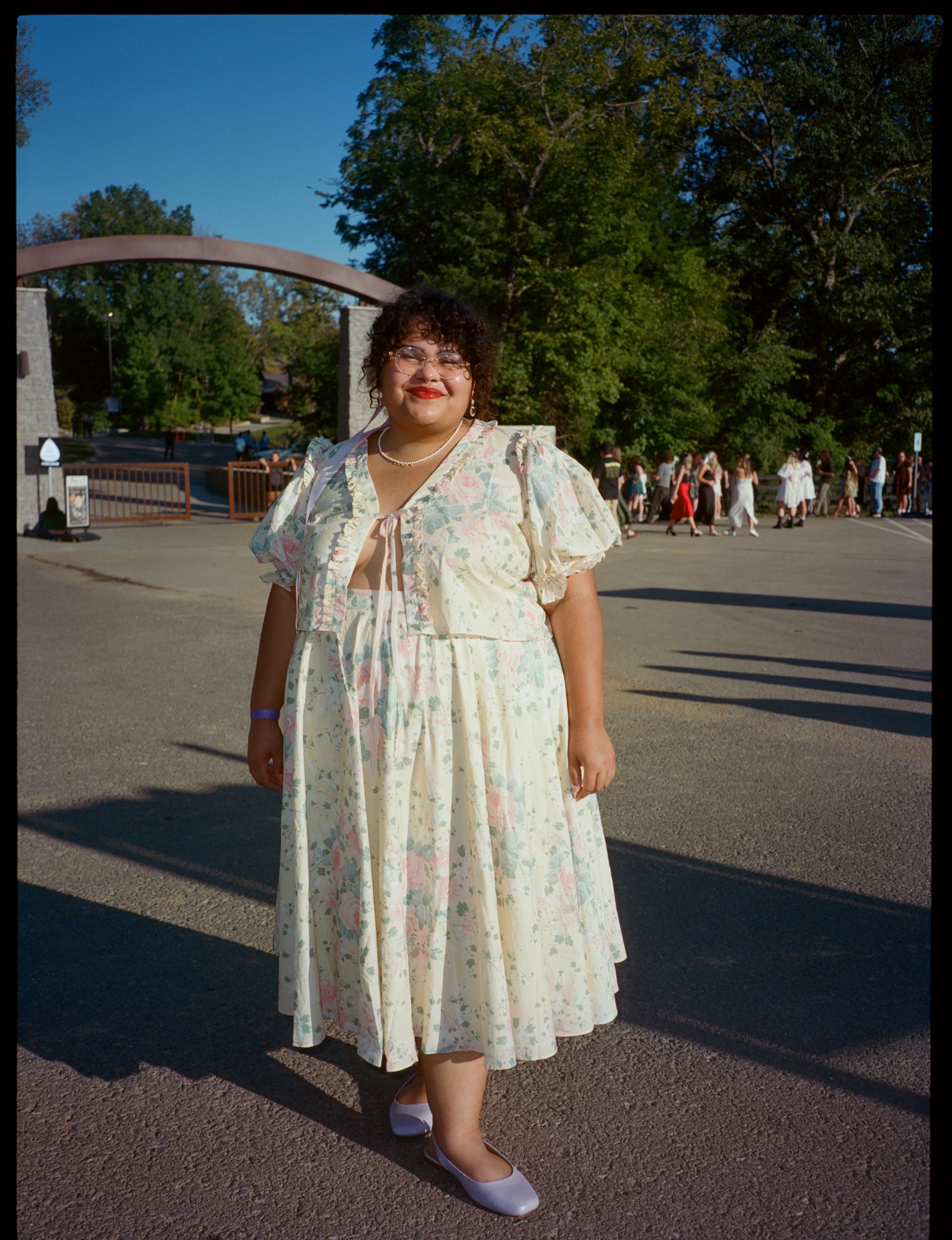 a lana del rey fan wears a matching skirt and shirt co-ord. she is smiling and has curly hair and is wearing red lip stick.