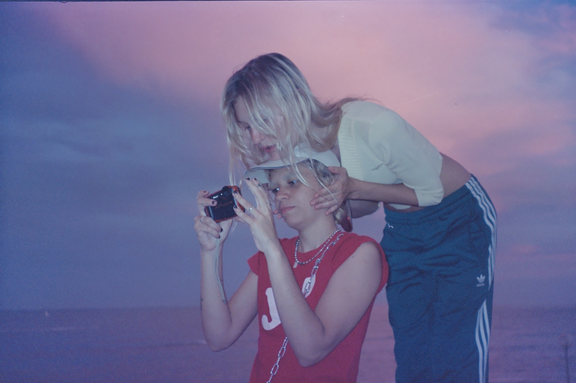 two friends looking at photos on a digital camera screen at sunset