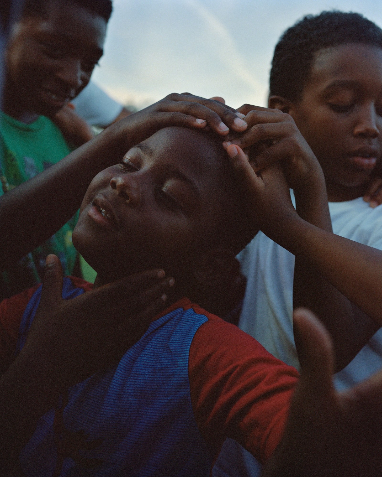 Photograph by Vasantha Yogananthan from Mystery Streets of a boy with other kids's hands on his face