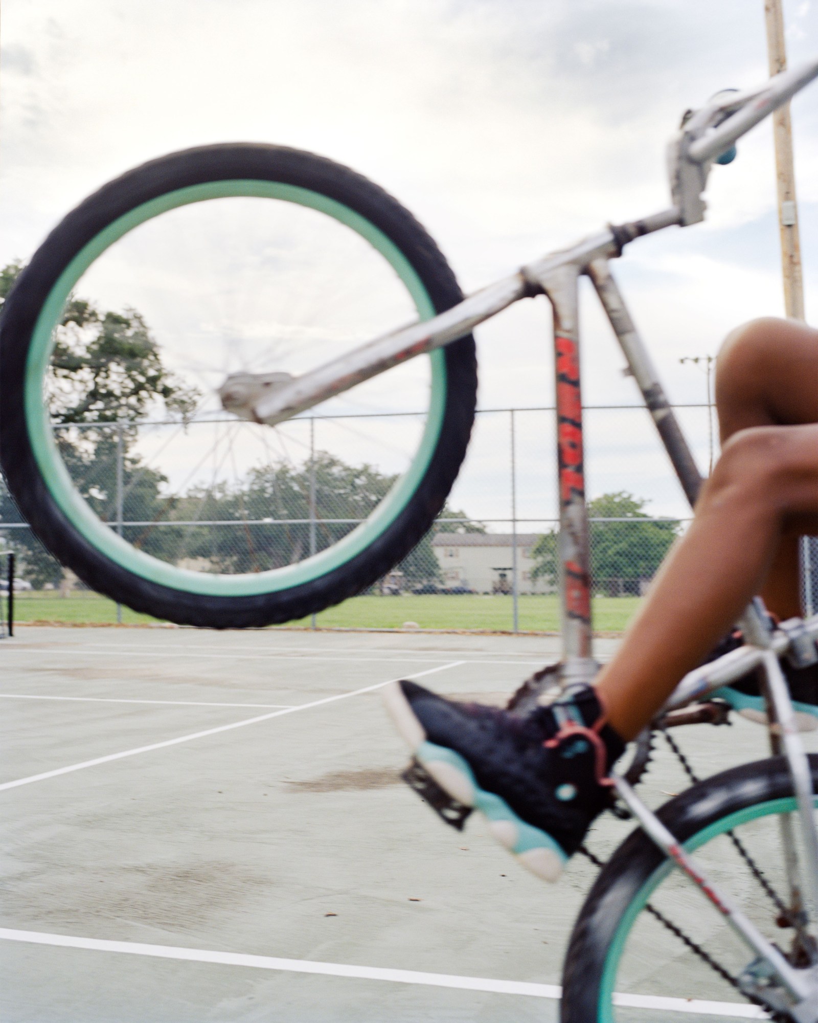 Photograph by Vasantha Yogananthan from Mystery Streets of the wheels of a bike ridden by a kid on a court