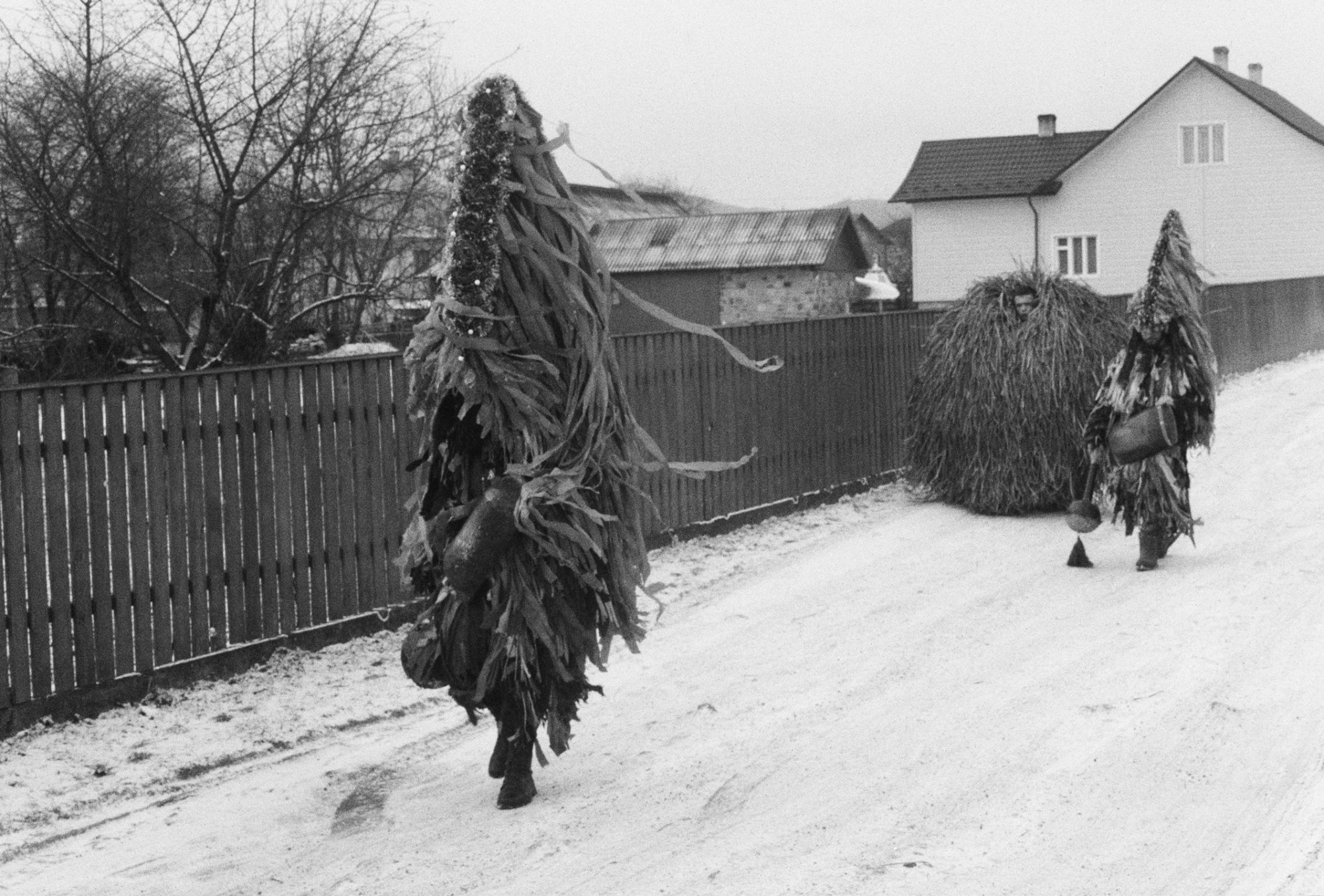 two people wearing tree-like homemade costumes walk down a snowy street in rural ukraine