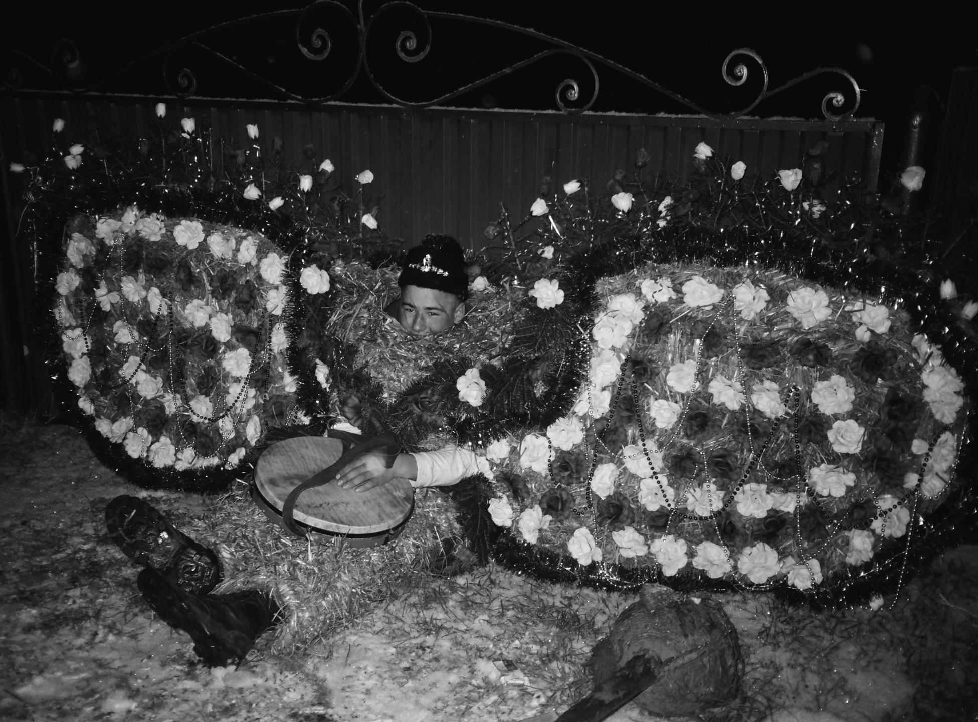 a man wearing a floral costume with large wing-like structure sits on the floor with a tambourine on his lap