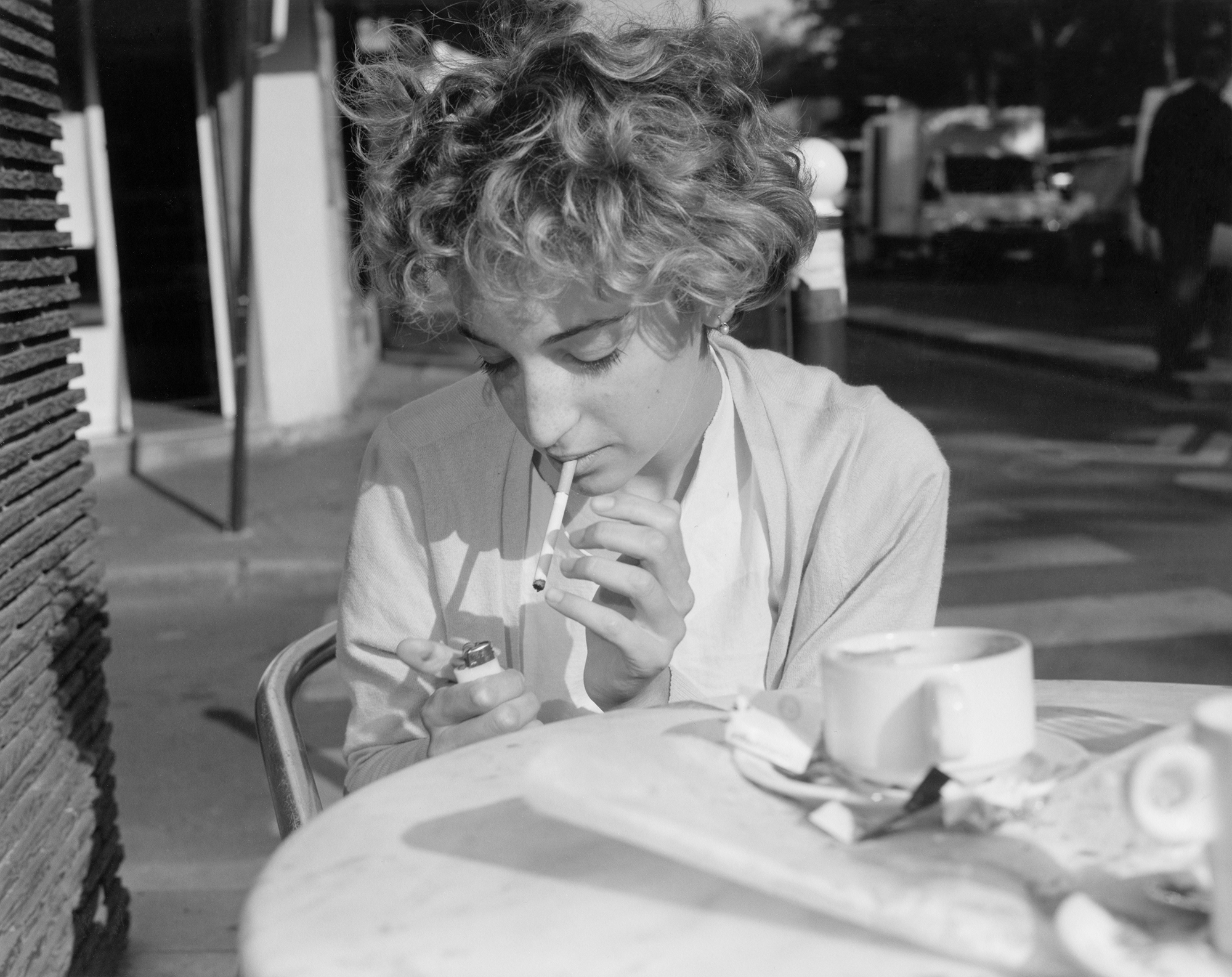 a blonde woman smoking cigarettes at a cafe table in paris