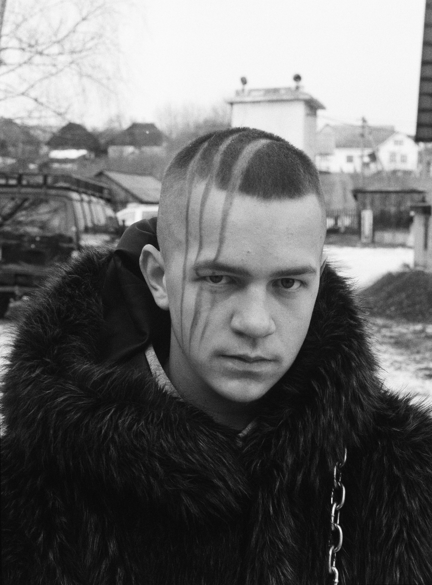 a young man wearing a fur coat has a fake bear-like scar down the side of his face, looking into the camera