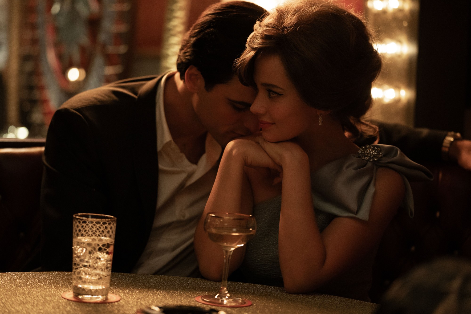 a photo of jacob elordi as elvis and cailee spaeny as priscilla in the a24 sofia coppola film. he wears a suit and is nestles into her neck. priscilla is wearing a silk blue dress and has her hair styled up.