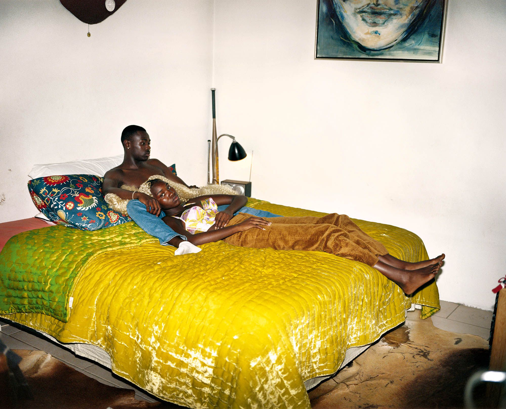 a young Black couple lay together on a colourful silk bedspread