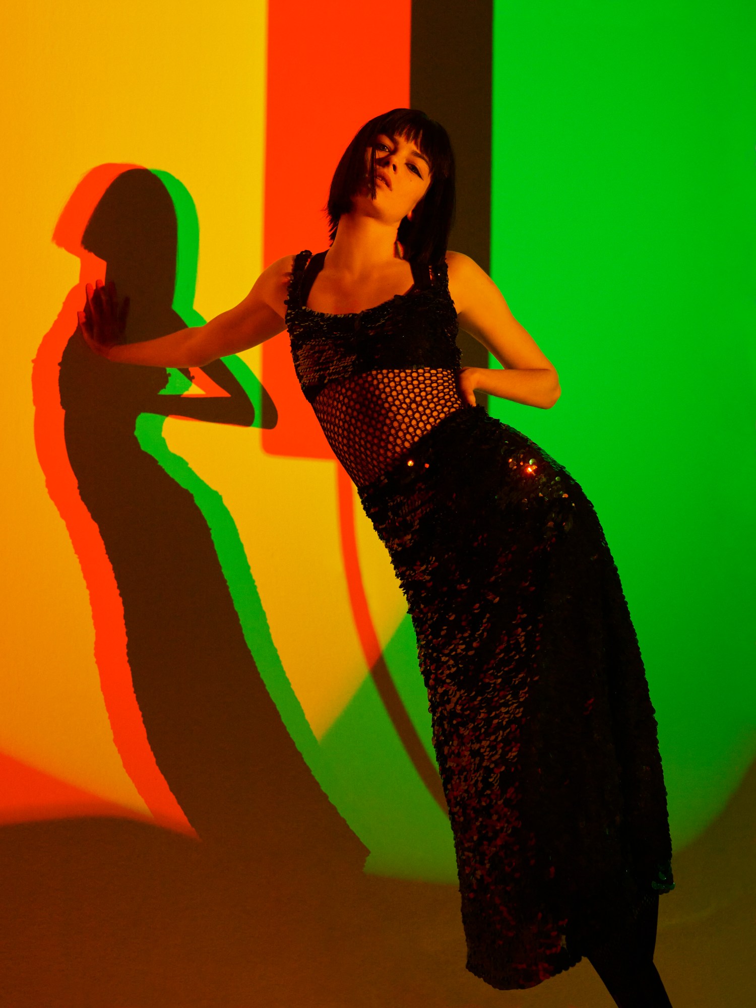 a woman in a black dress standing in front of a black, yellow, green and red background