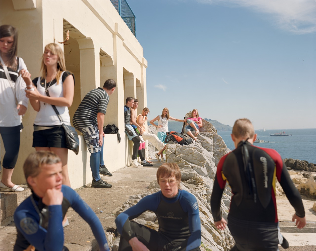 Photograph by Nick Waplington of those visiting the seaside, with divers and locals sitting on the rocks from The Corinthian Series