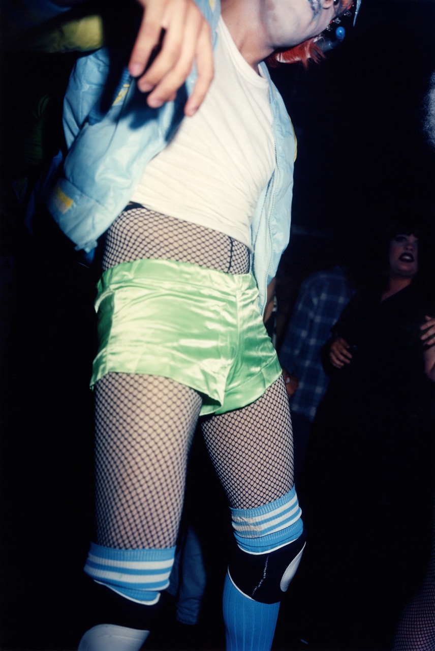 Photograph by Nick Waplington of a man in silk green shorts, fish nets, socks and rollerblading