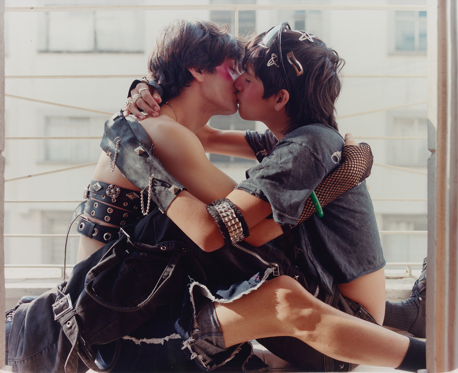 couple kissing in a window wearing fishnet gloves and belt buckles