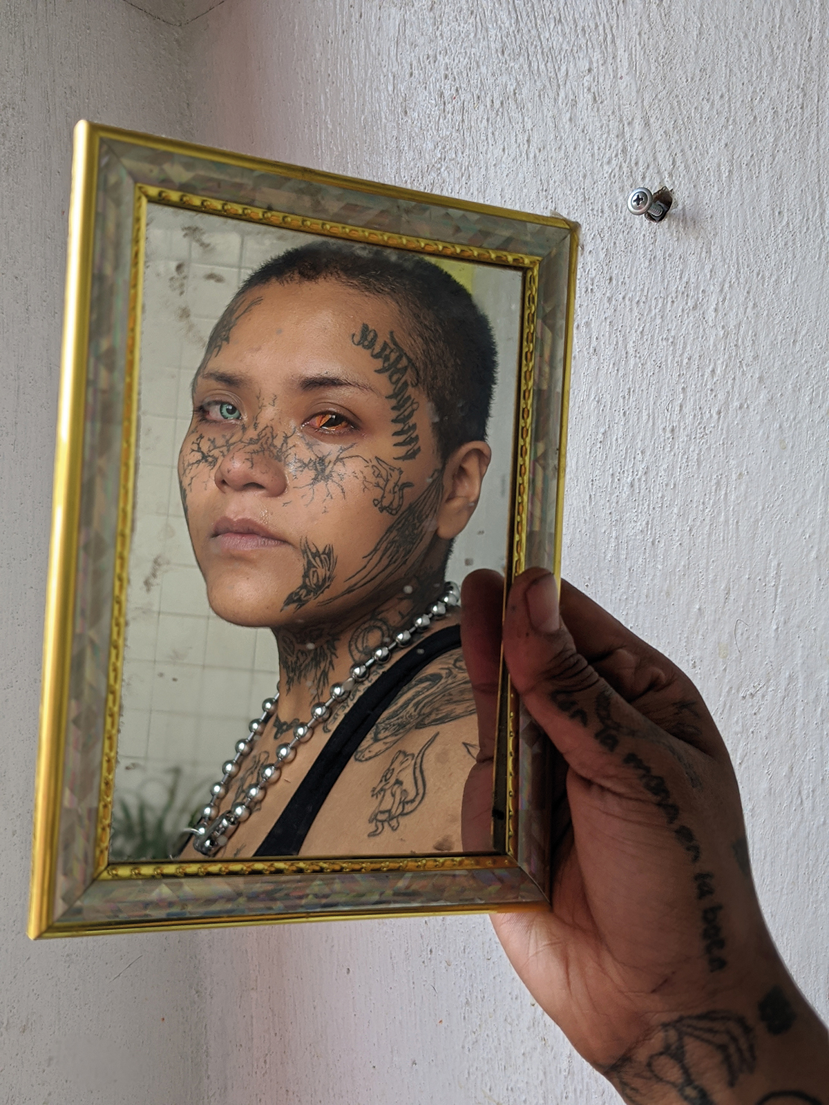 a tattooed hand holding a mirror reflecting a person with tattoos