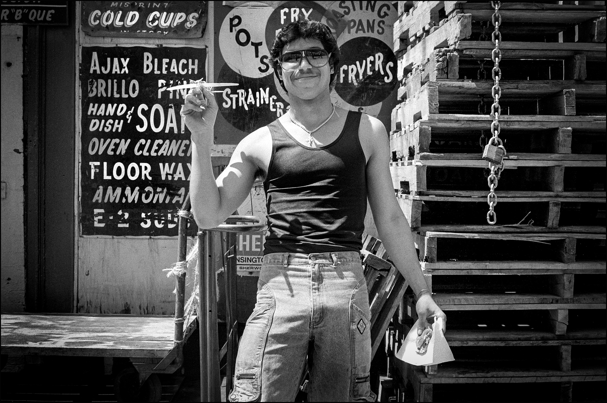 A young Puerto Rican wearing shades holds a toy airplane while in the background, signs advertise cleaning products for sale