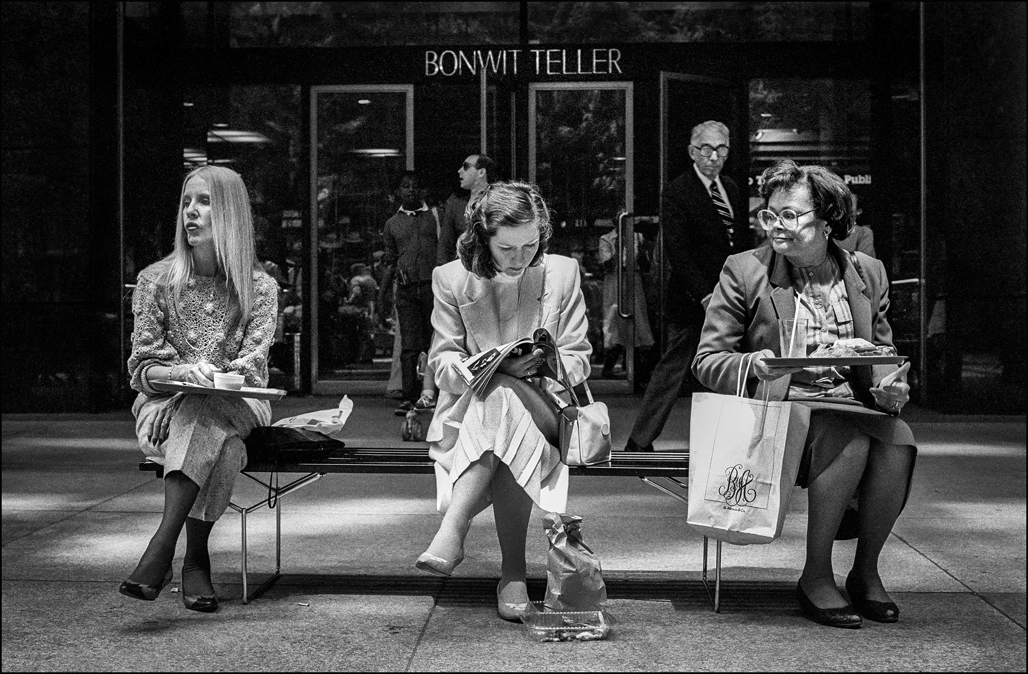 three women take their lunchbreak on a bench outside bonwit teller, a replacement store was built as part of the new skyscraper on the ground floor.