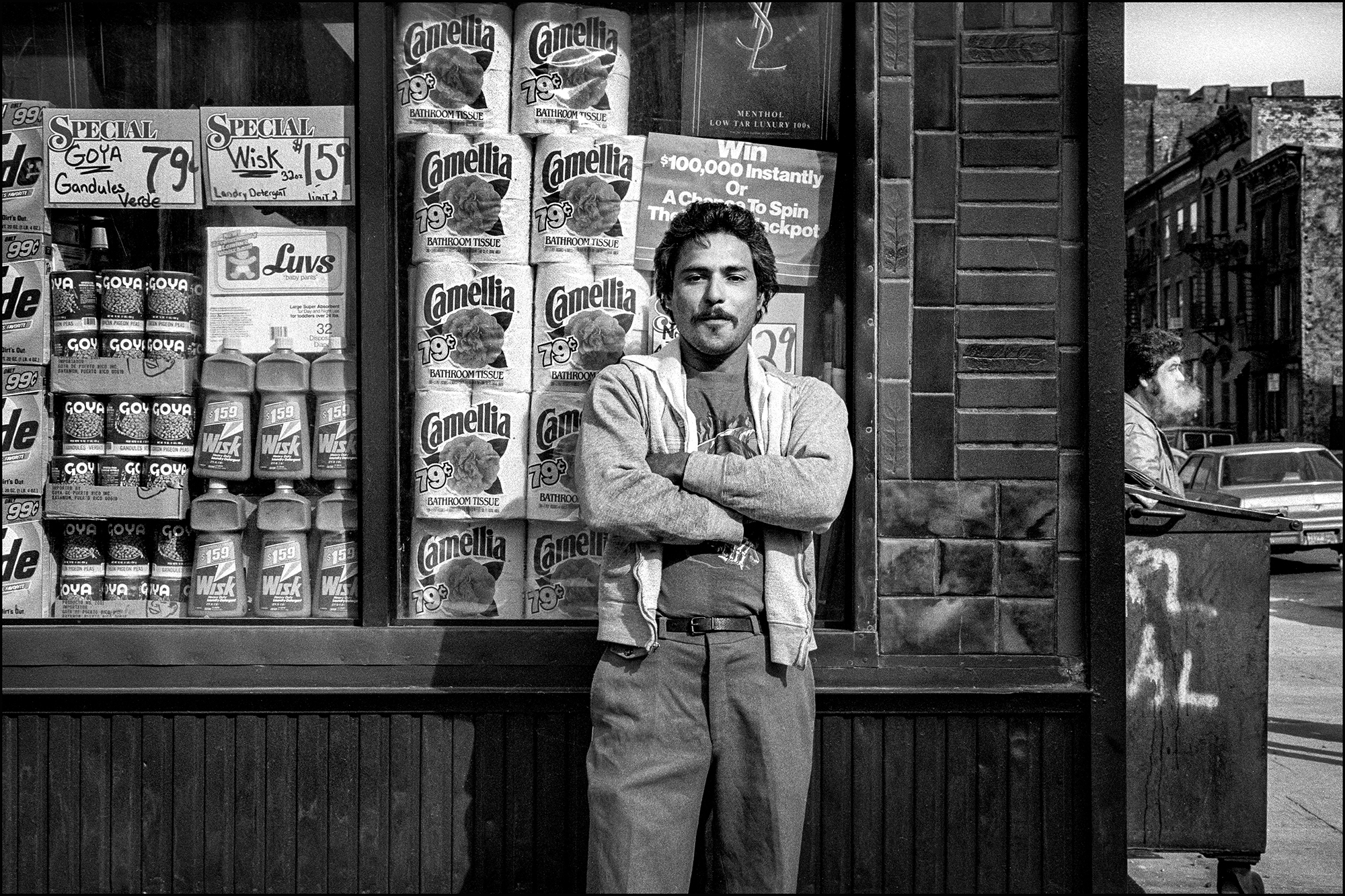 A young man strikes a pose outside a local street shop in the Lower East Side. A tantalizing sign promising the chance to win a fortune, while around the corner, a man leisurely savours his smoke.