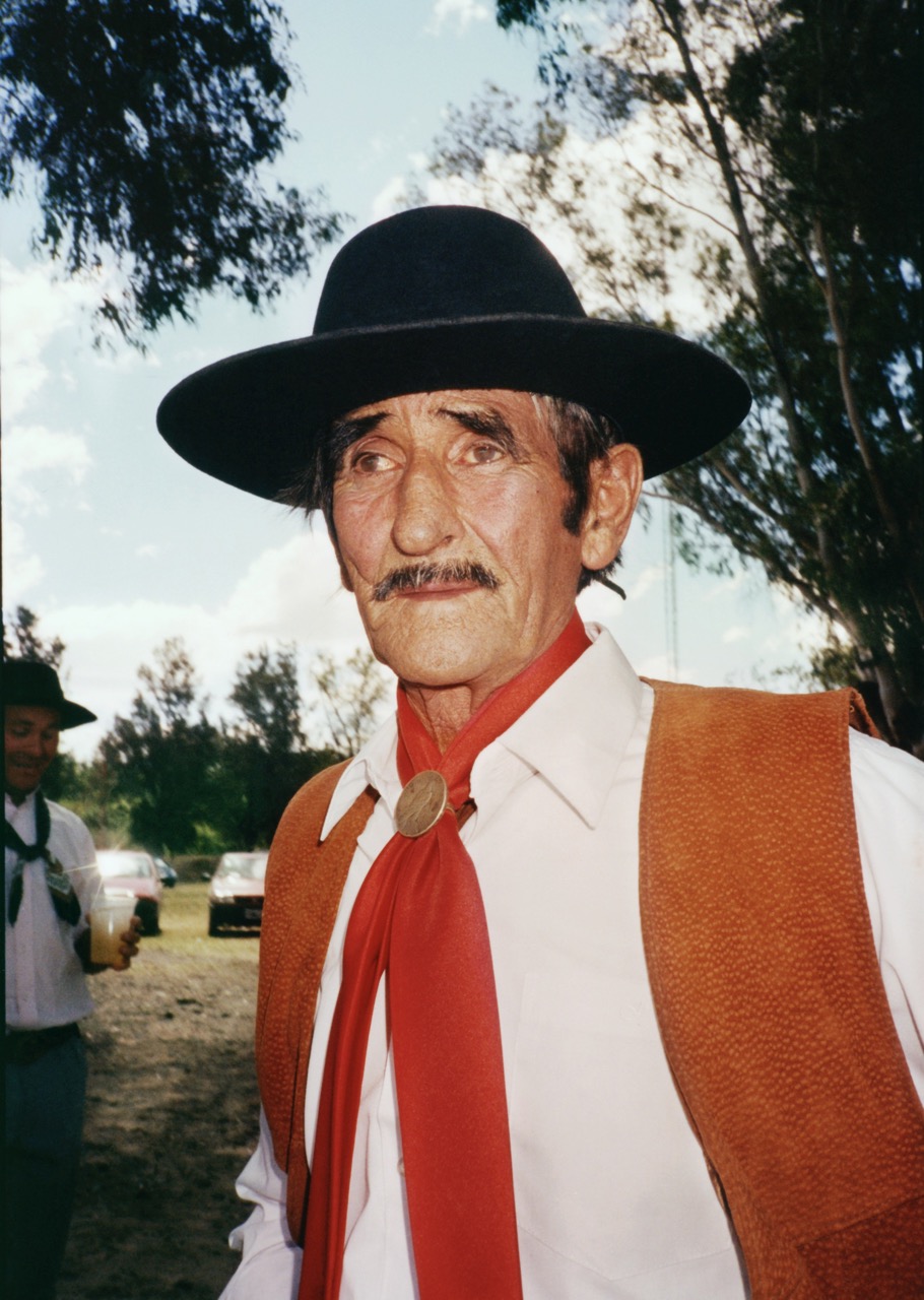 an older gaucho in a red tie, orange vest and black hat