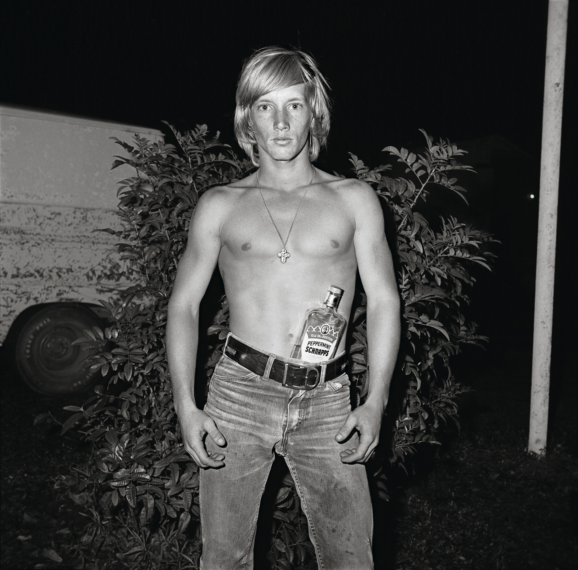 black-and-white image of a topless man with schnapps bottle in his jeans