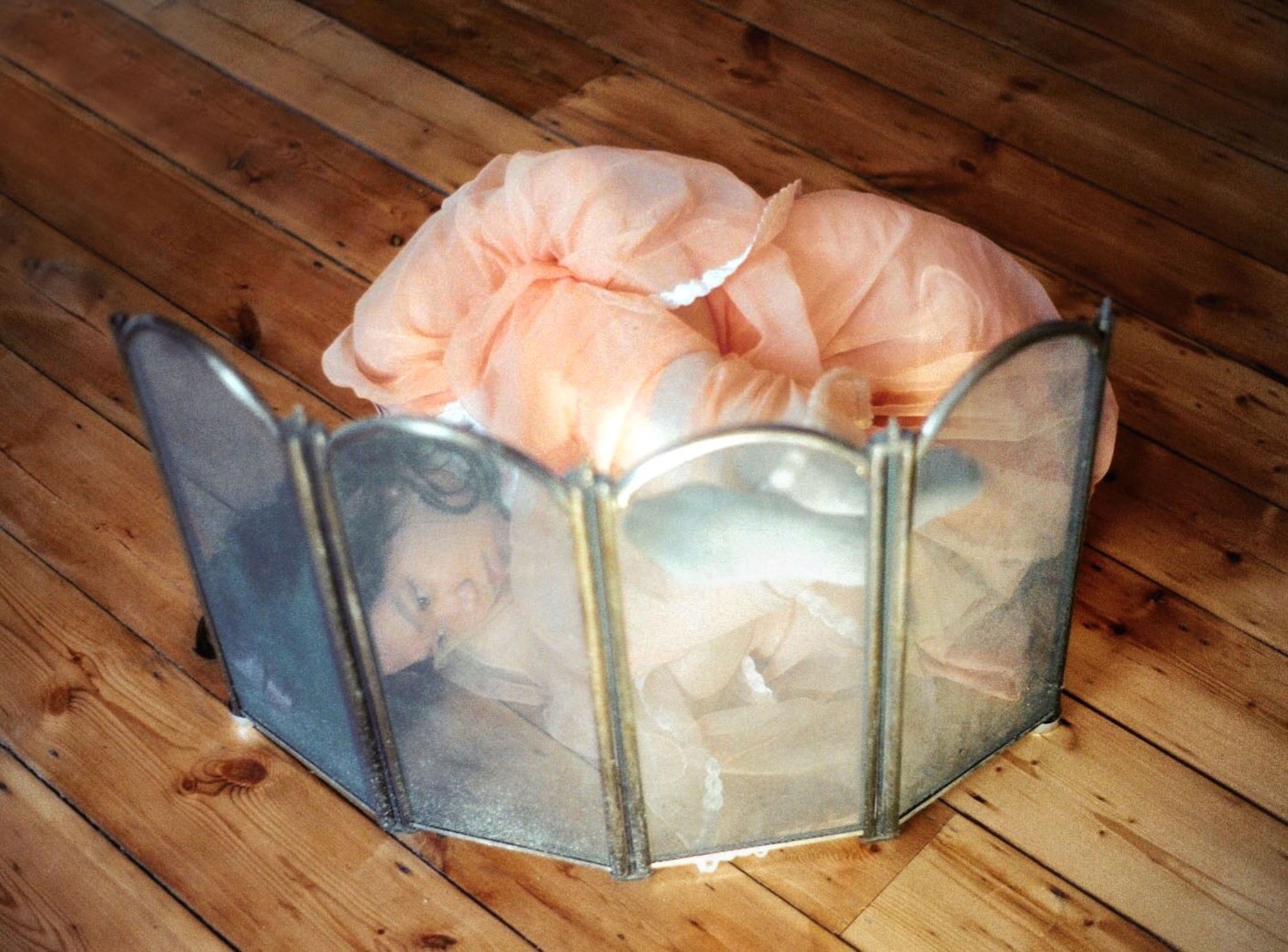 a woman curled up against a fire grate on a wood floor wearing a pink dress