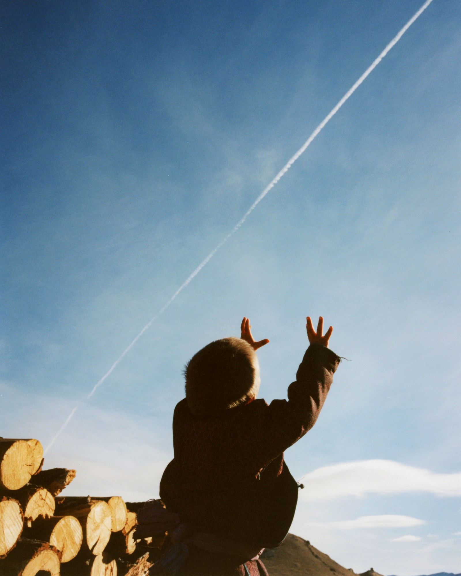 a young child in a fur hat reaching for a plane leaving white smoke in it's wake