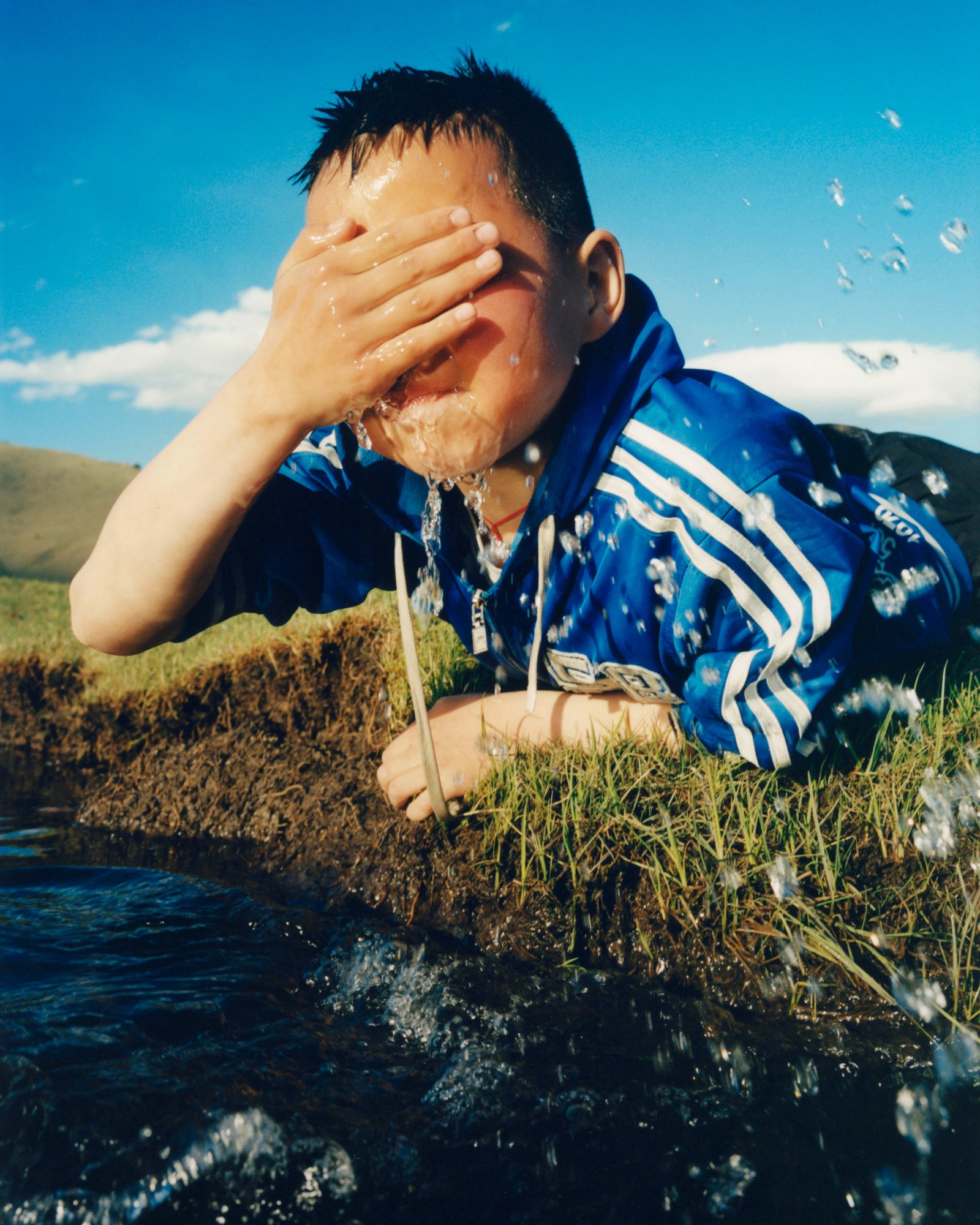 a young boy in a blue jersey splashing water on his face