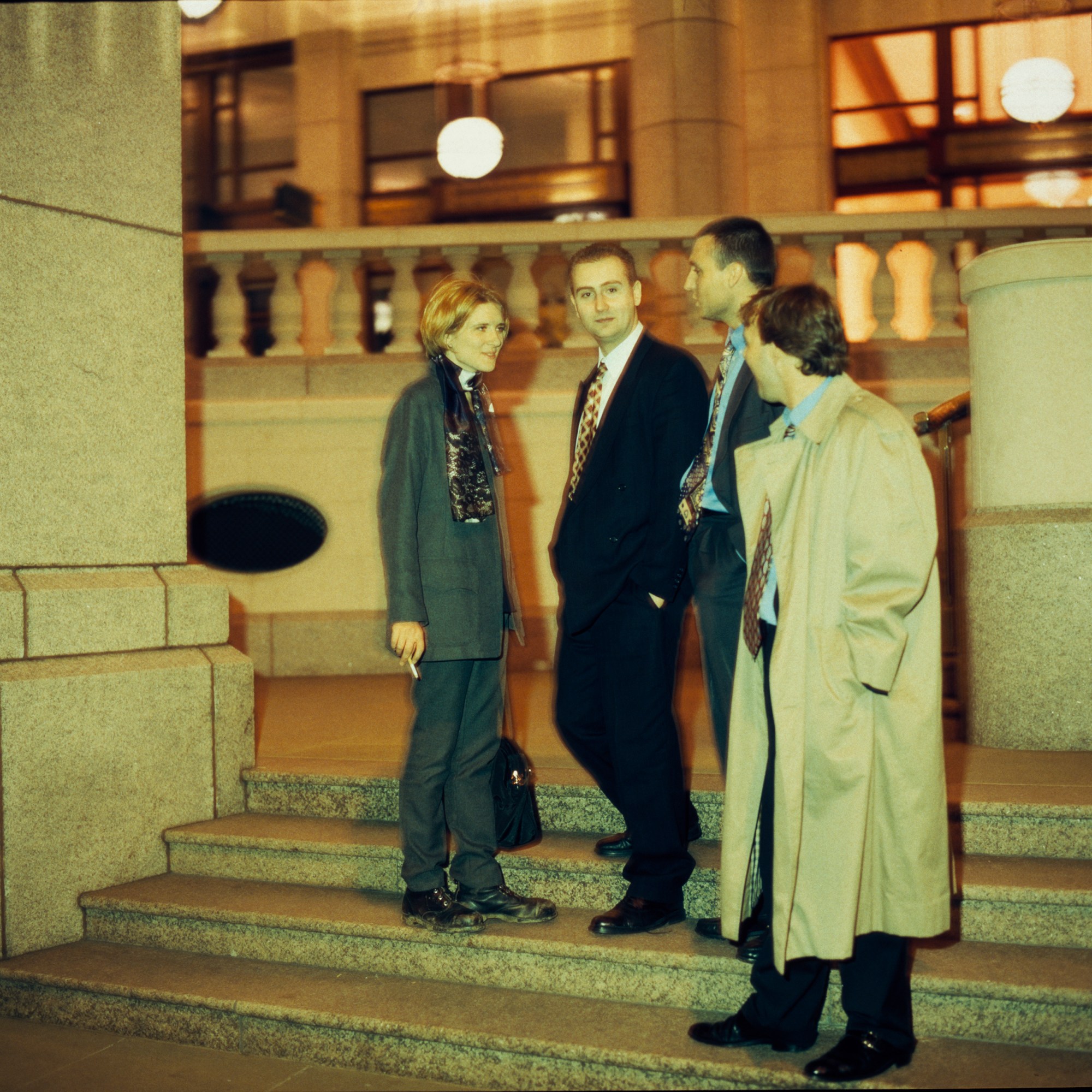 one woman talking to three men on the stairs of a large building