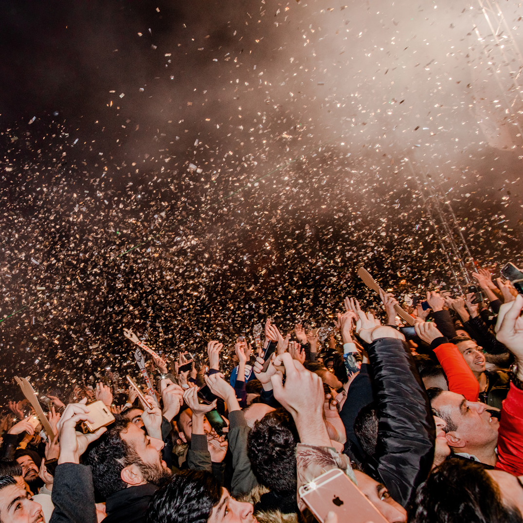 A crowd of people holding their hands up in the air as confetti rains down on them