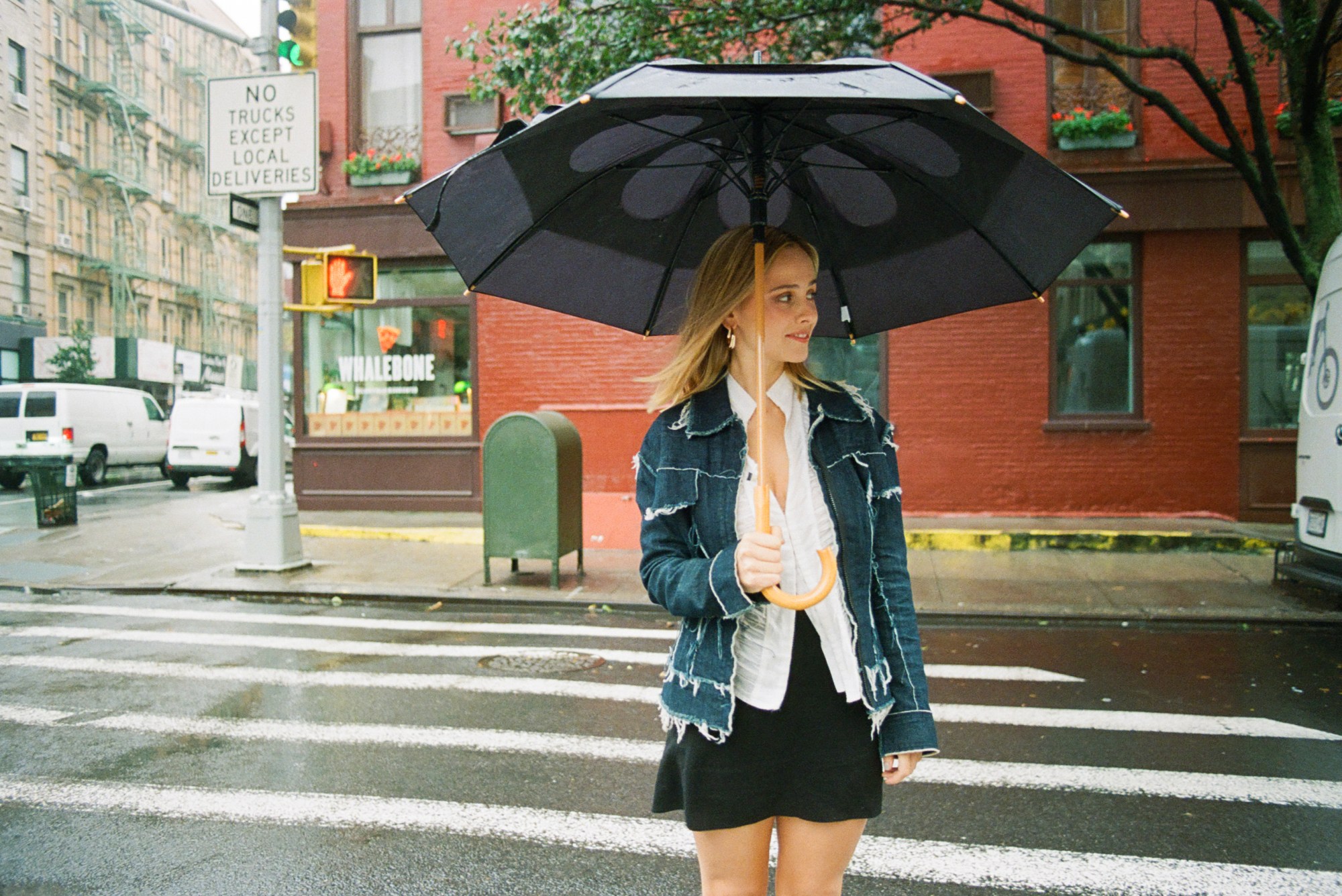 a portrait of pauline chalamet on the sreets of new york. she has blonde shoulder length hair and is white. she wears a denim jacket and black skirt and is carrying an umbrella