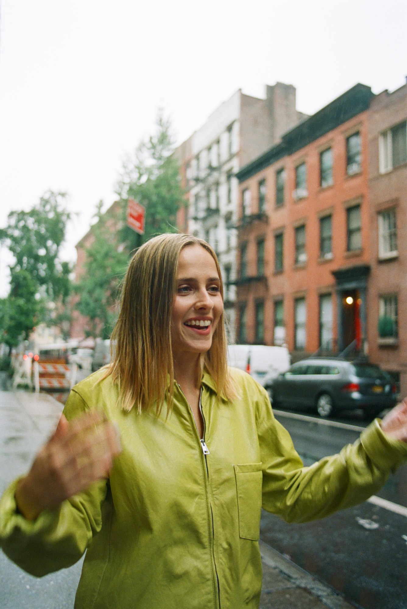 pauline chalamet wearing a green zip up jacket in the street of new york smiling. she has shoulder length blonde hair