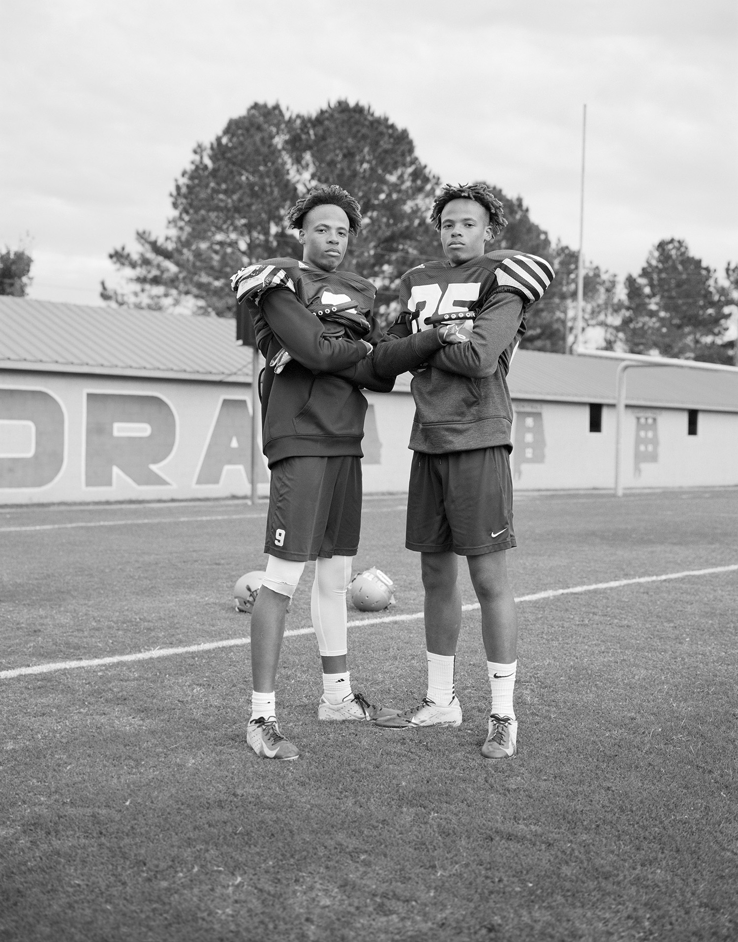 twin teenage American football players stand side-by-side, arms crossed, on the pitch