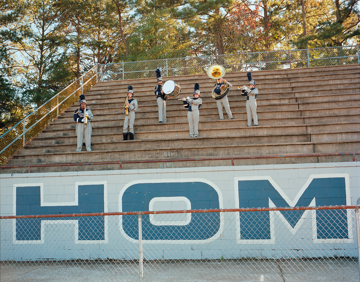 six members of a brass band stand on the bleachers during golden hour playing their instruments