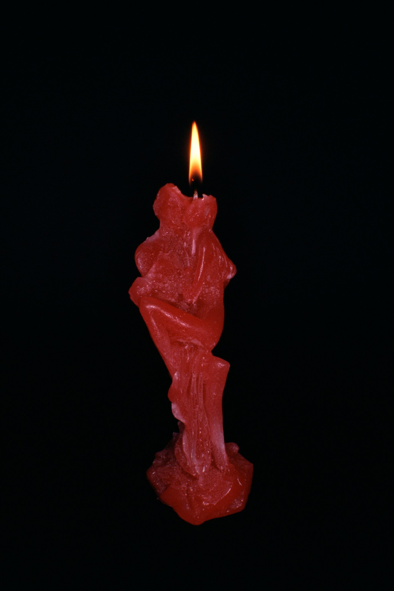 a lit, half-burnt red wax candle in the form of a lovers' embrace