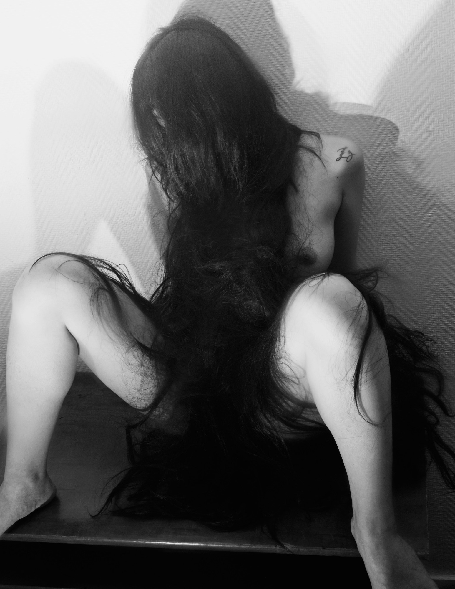 a woman with long hair sits with her legs open and hair reaching down over her crotch