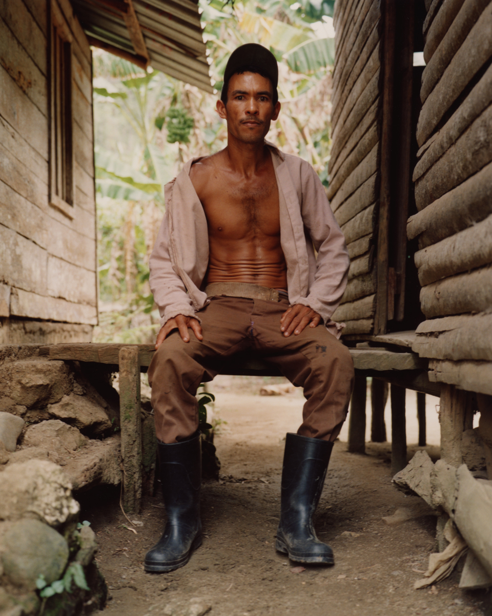 a man in an open oxford and black boots sitting on a handmade bench