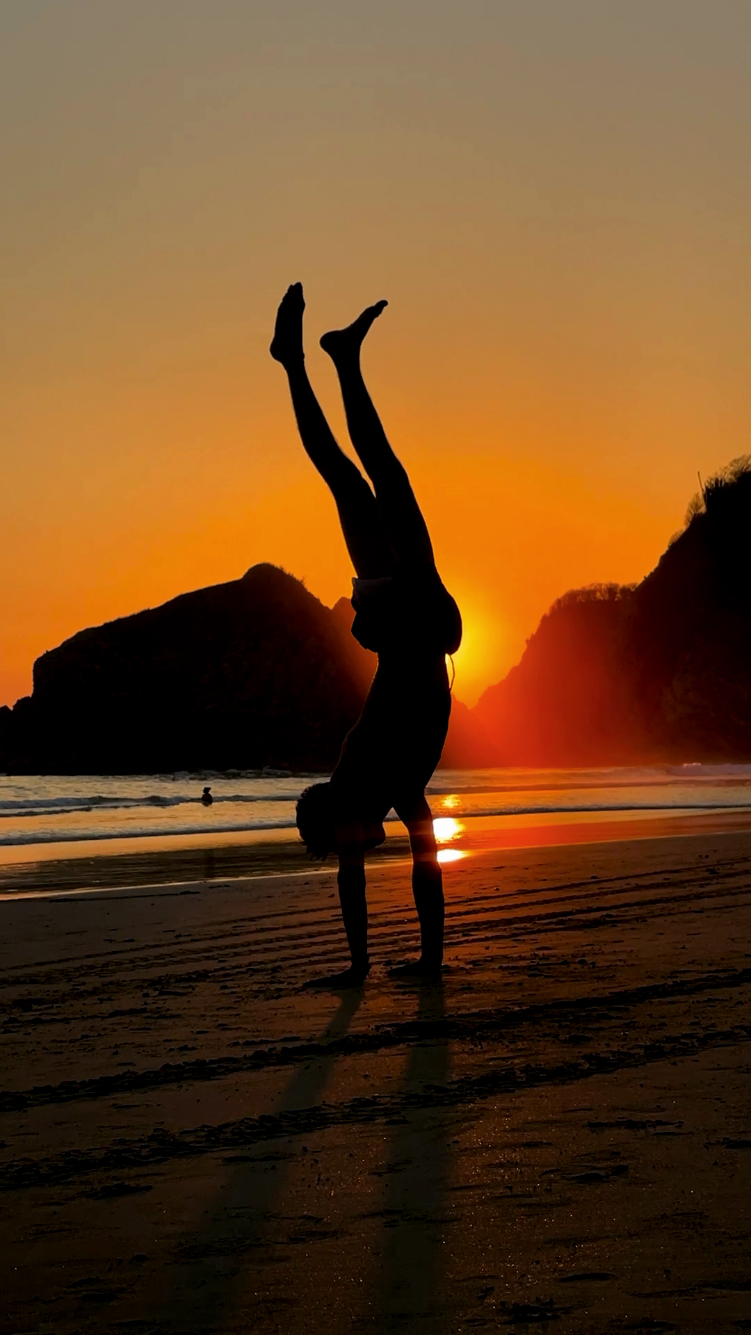 a boy's silhouette doing a handstand on the beach