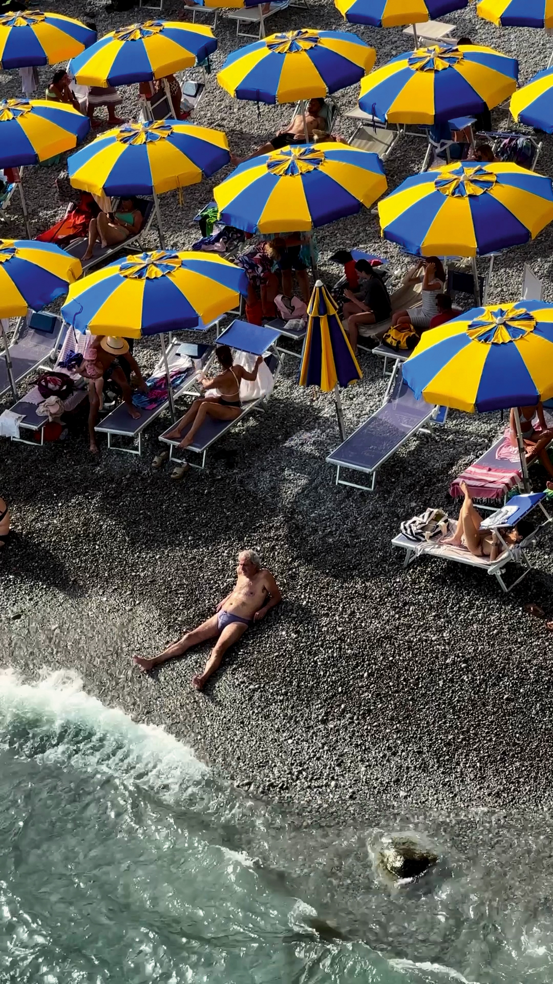 people lying on deck chairs on a black pebbly beach