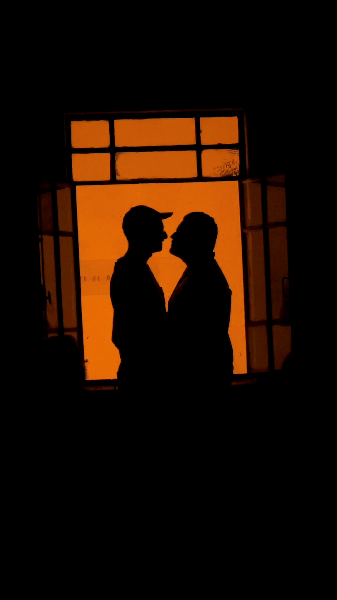 the silhouette of two men leading in to kiss one another framed through a window