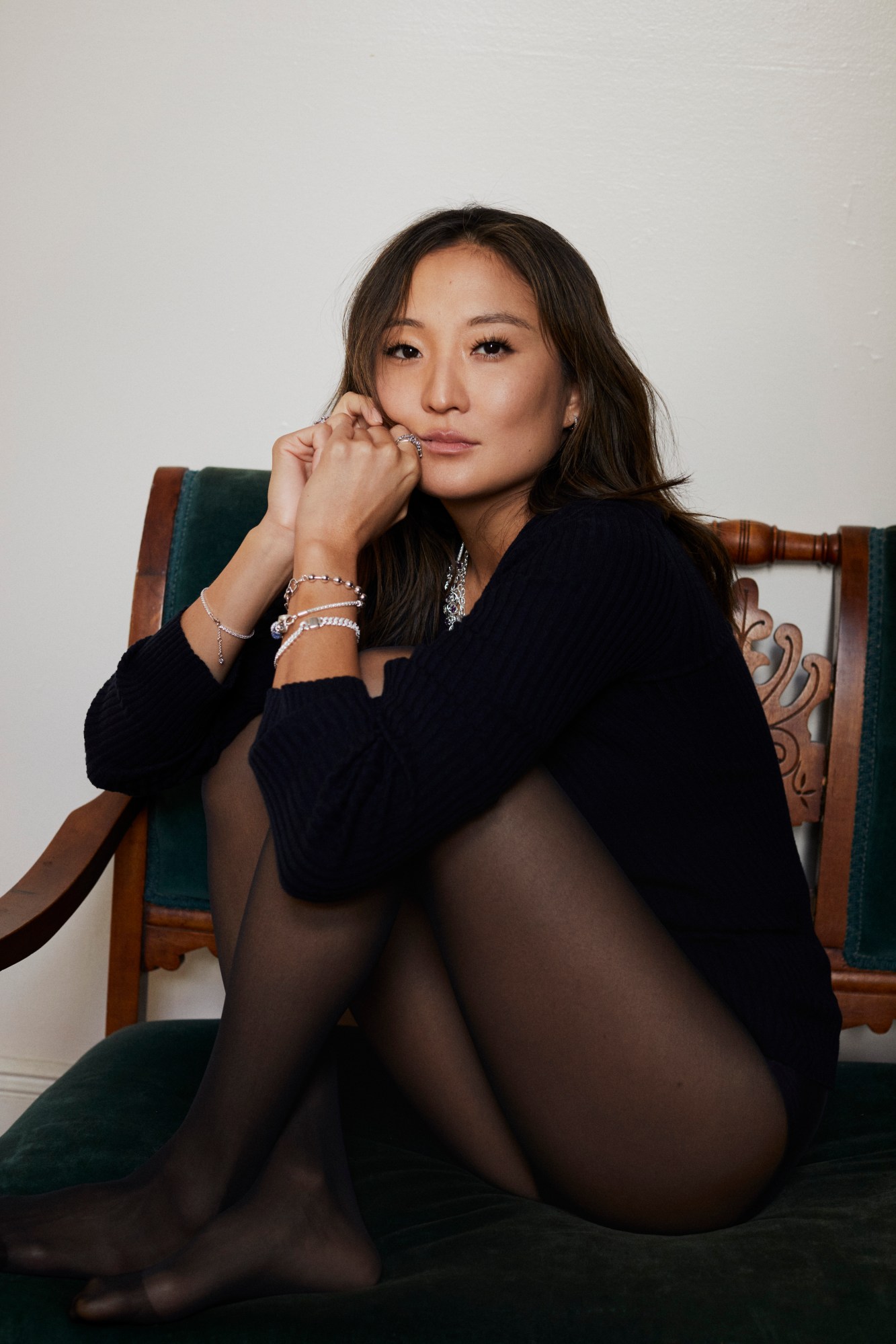 Ashley Park sitting on a chair in black tights and black jumper