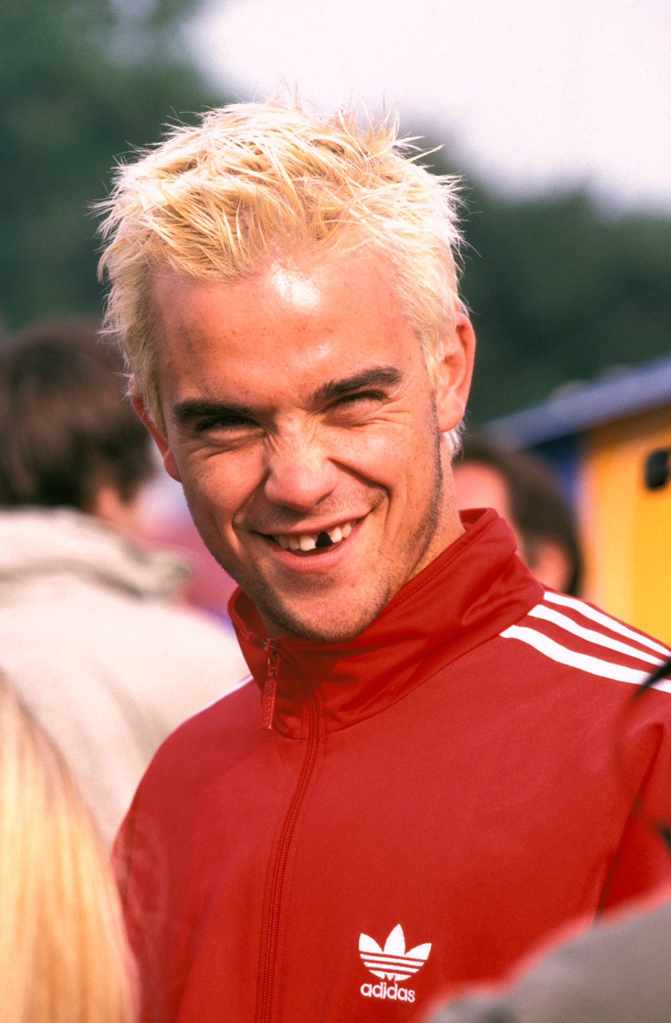 a headshot of robbie williams with bleached hair and an adidas sweatshirt