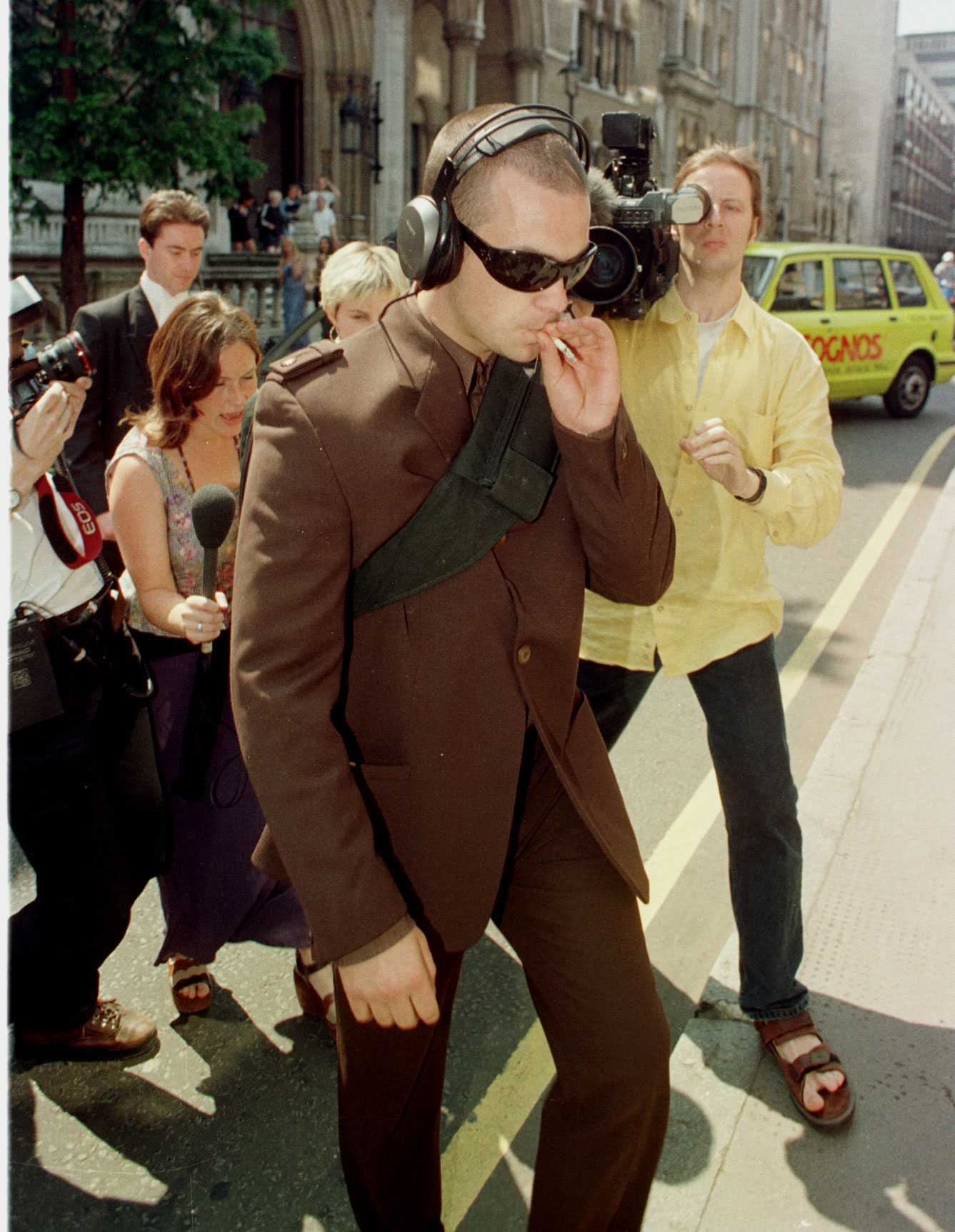 robbie williams in a brown suit walking into court in 1997; paparazzi and reporters surround him