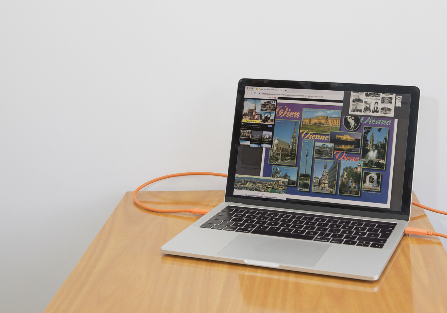 a laptop on a glossy wooden table; on the screen is a collage of vienna postcard shots